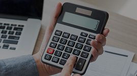 #PraCegoVer Texto: RENEGOCIAÇÃO DE DÍVIDAS. Imagem: mãos masculinas seguram uma calculadora. Ao fundo da imagem, há uma mesa com notebook aberto e alguns papéis.